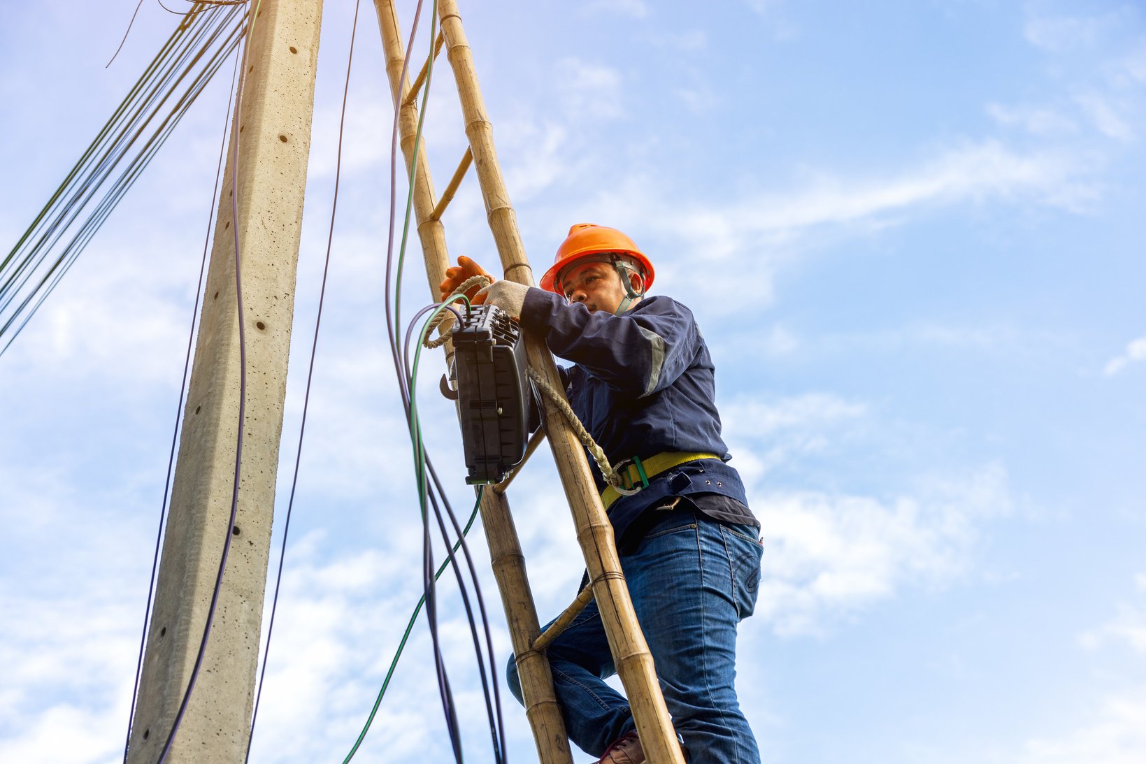 A telecoms worker is shown working from a utility pole ladder wh